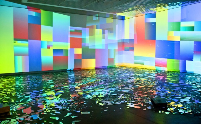 An image of a room with walls covered in a multicolored abstract pattern of squares and rectangles. The floor is patterned also.